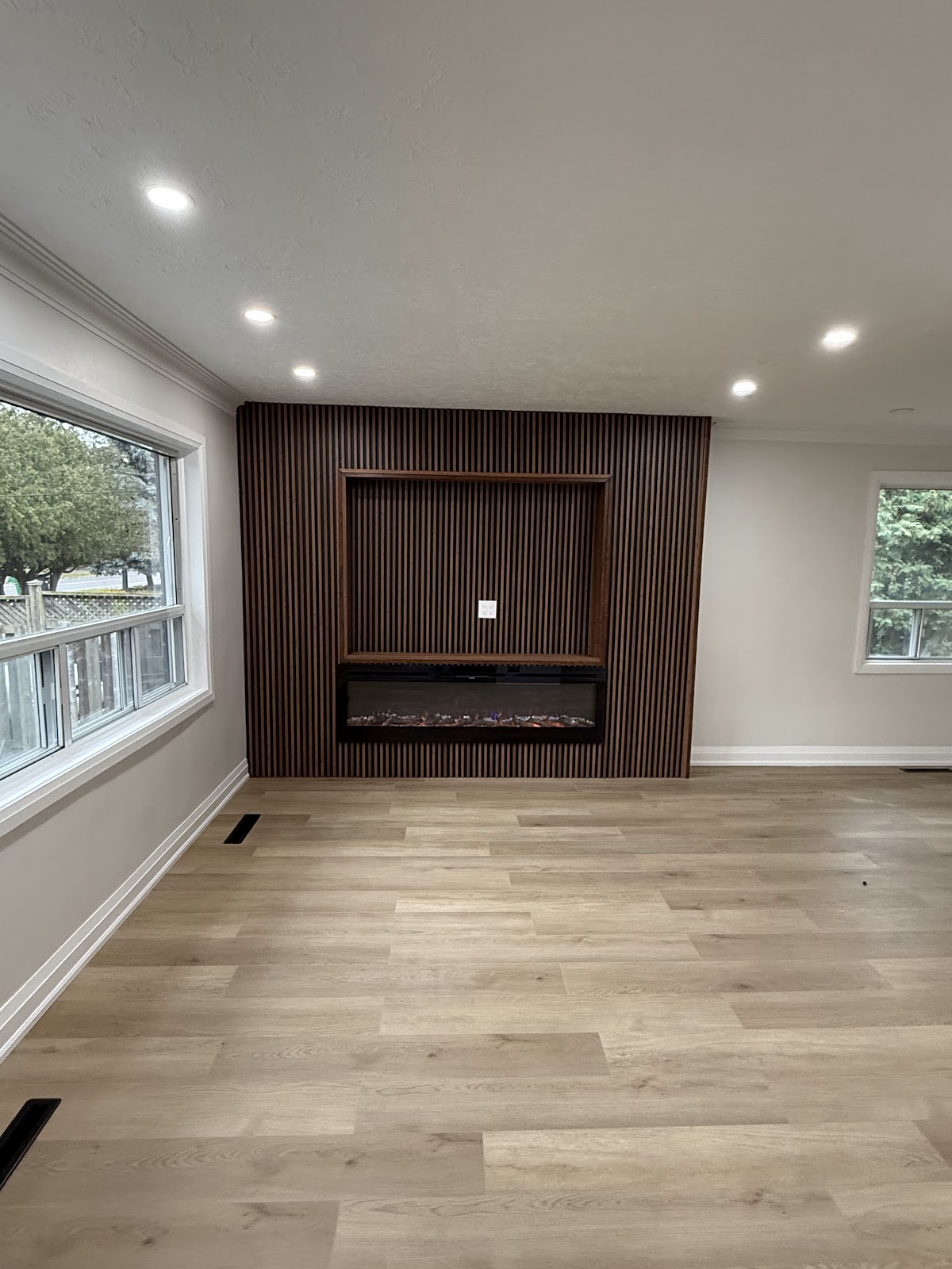 Renovated living room with wood slat feature wall, electric fireplace, TV niche, and new vinyl plank flooring