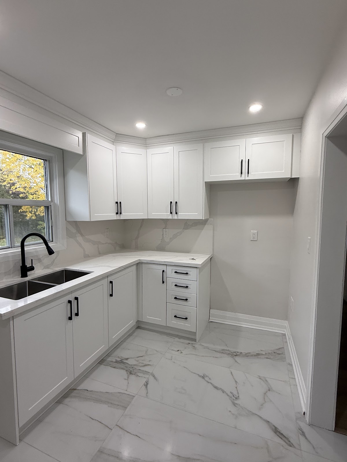Newly renovated kitchen with white shaker cabinets, black handles, and marble-look tile floor and backsplash